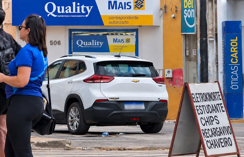 Carro estacionado junto à calçada em rua comercial movimentada